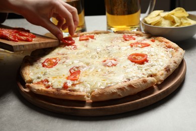Woman putting tomato onto pizza Margherita at table, closeup
