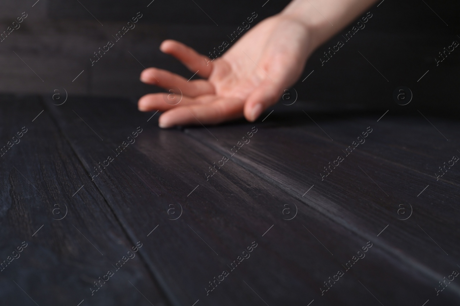 Photo of Woman holding hand above black wooden table, selective focus. Space for text