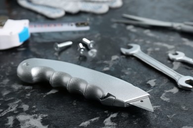 Photo of Utility knife and different tools on black textured table, closeup