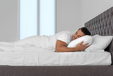 Photo of Young man sleeping in bed with soft pillows at home