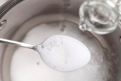 Pouring vinegar into spoon with baking soda over saucepan, closeup