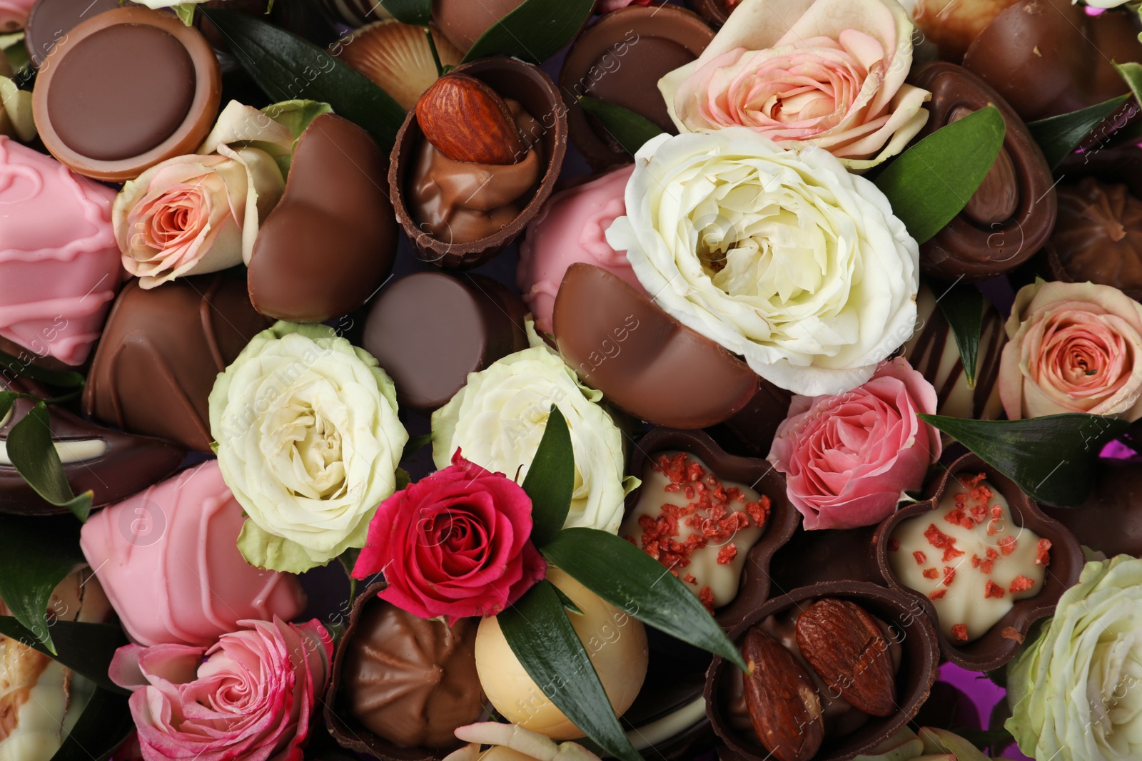 Photo of Beautiful bouquet of flowers and chocolate candies as background, closeup