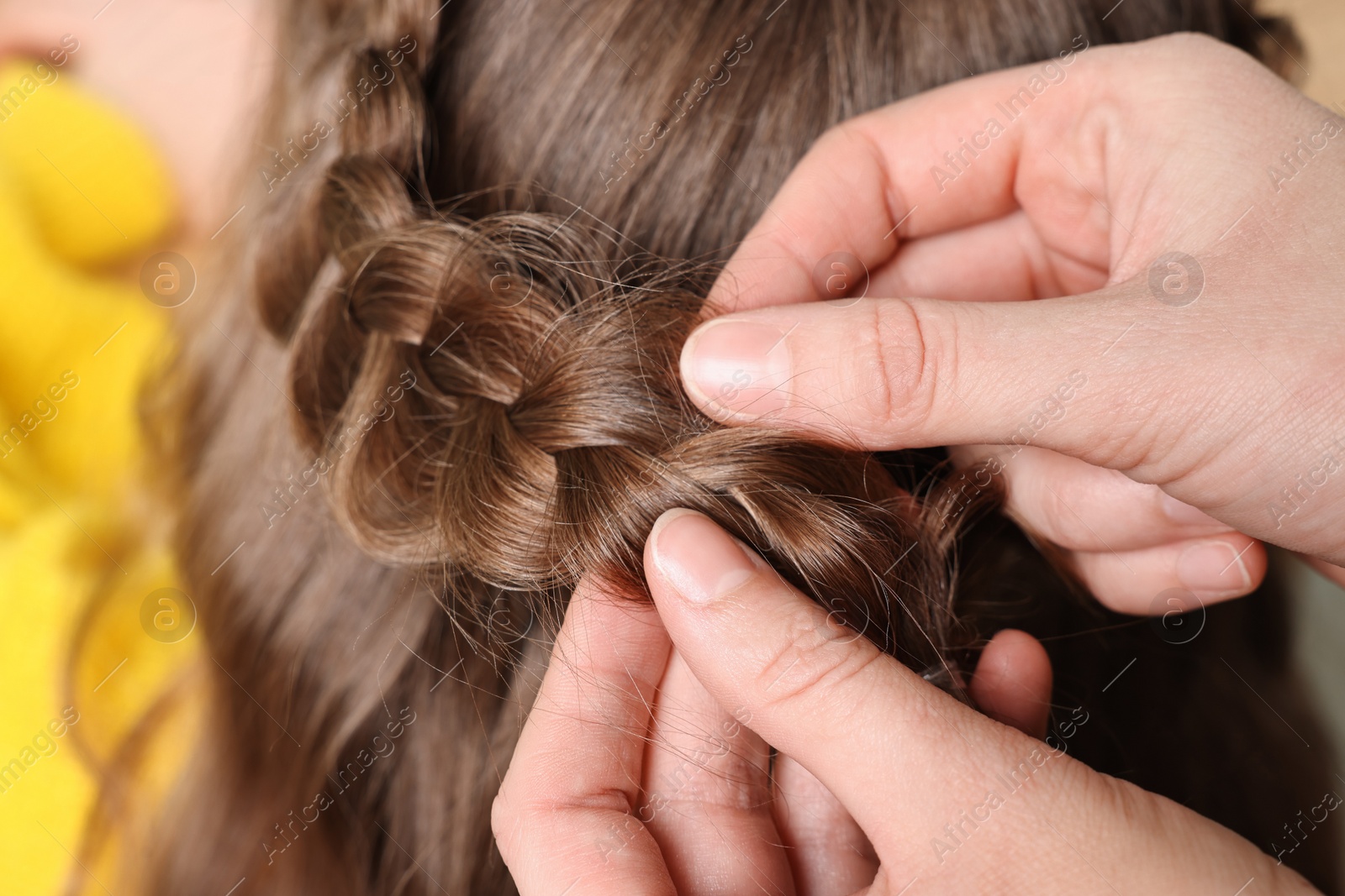 Photo of Professional stylist braiding girl's hair indoors, closeup