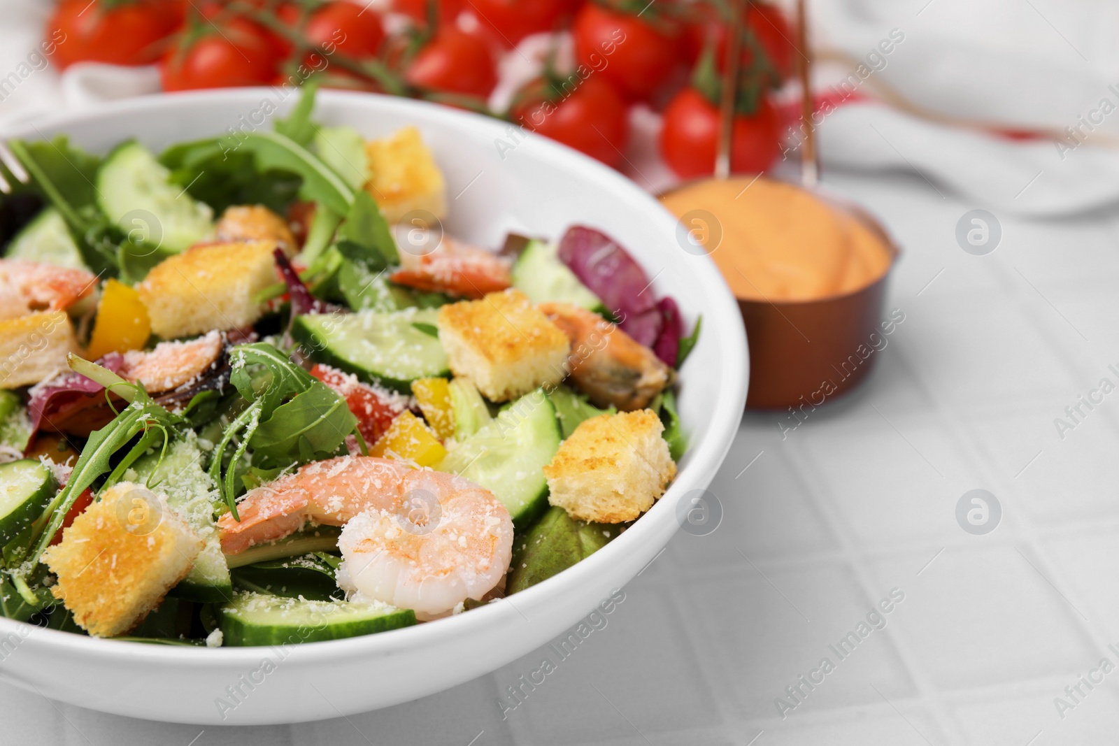 Photo of Delicious salad with croutons, cucumber and shrimp served on white tiled table, closeup. Space for text