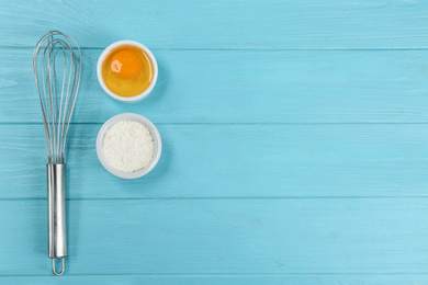 Photo of Raw egg, flour and whisk on light blue wooden table, flat lay with space for text. Baking pie