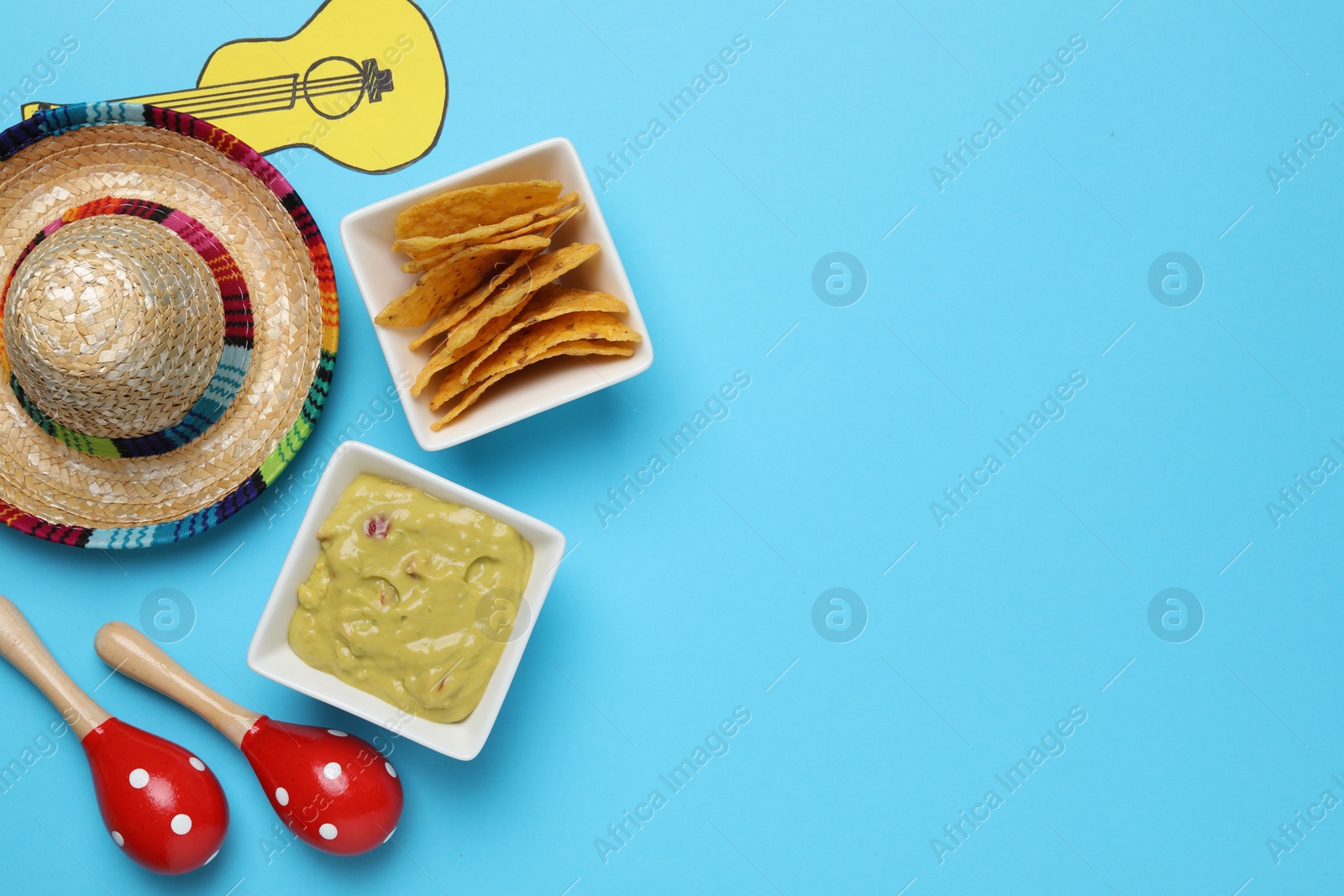 Photo of Mexican sombrero hat, guacamole, nachos chips, maracas and paper guitar on light blue background, flat lay. Space for text