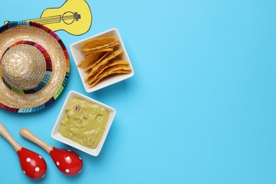 Mexican sombrero hat, guacamole, nachos chips, maracas and paper guitar on light blue background, flat lay. Space for text