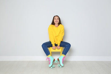 Young woman with roller skates sitting on chair near color wall