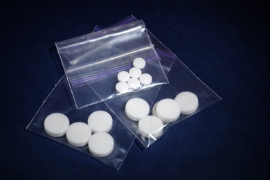 Ecstasy pills in plastic bags on color background