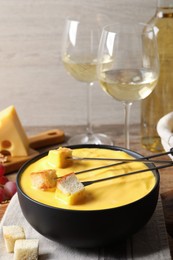 Photo of Tasty cheese fondue, forks with bread pieces and wine on table