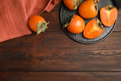 Photo of Tasty ripe persimmons on brown wooden table, flat lay. Space for text