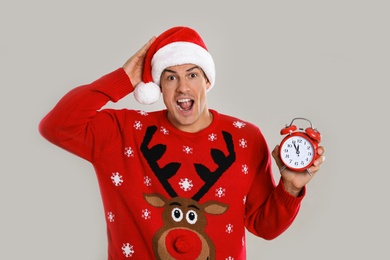 Photo of Man in Santa hat with alarm clock on grey background. Christmas countdown