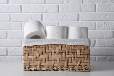 Photo of Toilet paper rolls in wicker basket on white table against brick wall