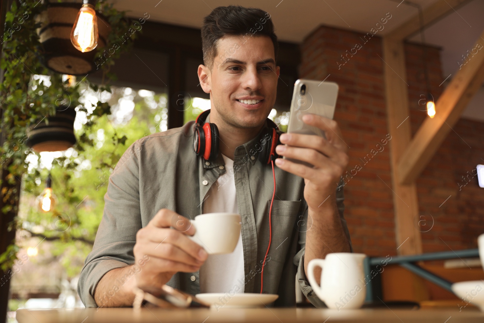 Photo of Handsome man with cup of coffee and smartphone at cafe in morning