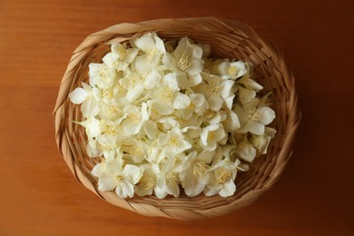 Photo of Beautiful white jasmine flowers in wicker basket on wooden table, top view
