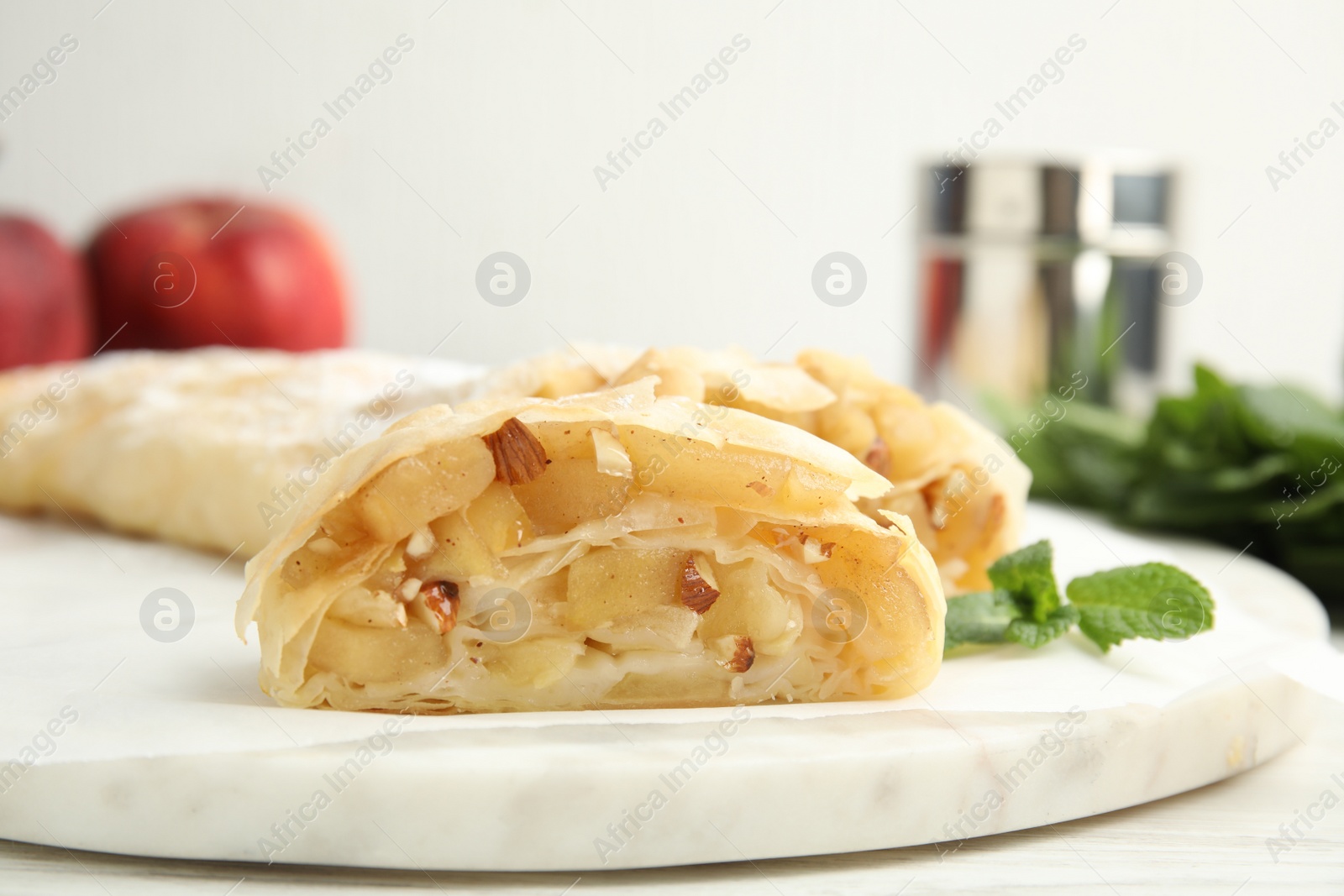 Photo of Delicious apple strudel with almonds and mint on white board, closeup