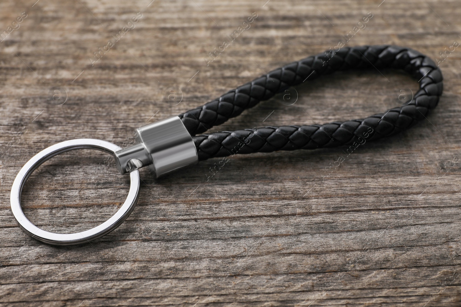 Photo of Black leather keychain on wooden background, closeup