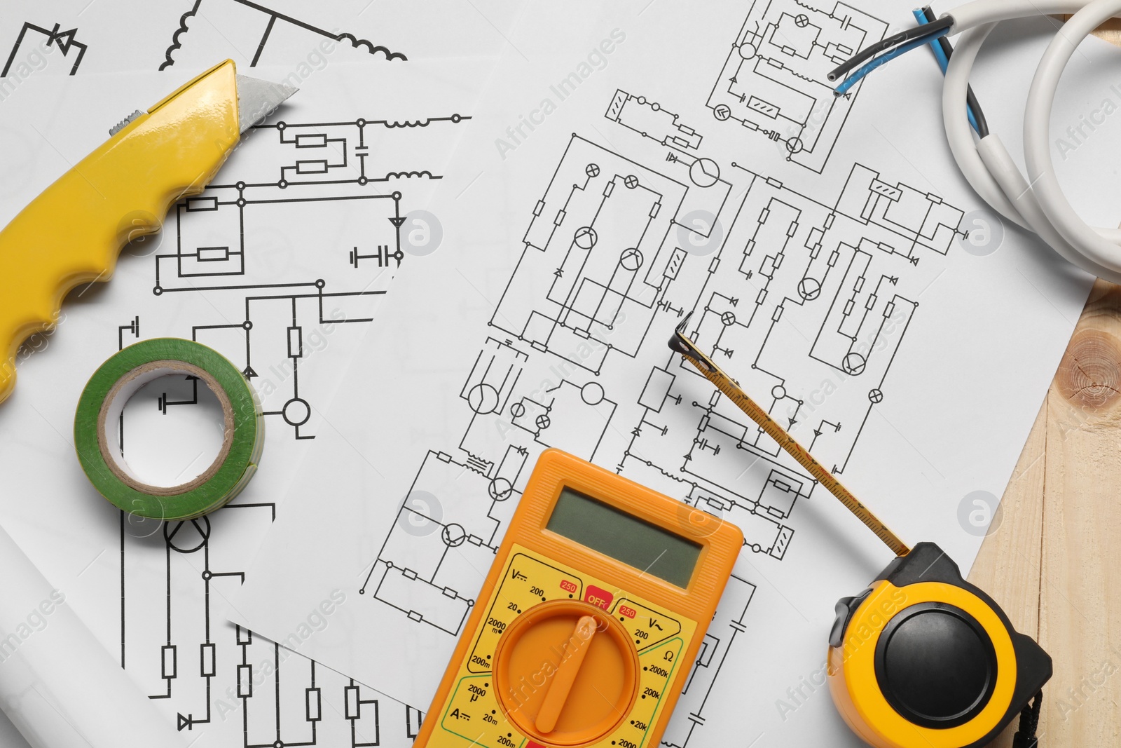 Photo of Wiring diagrams, wires and digital multimeter on wooden table, top view