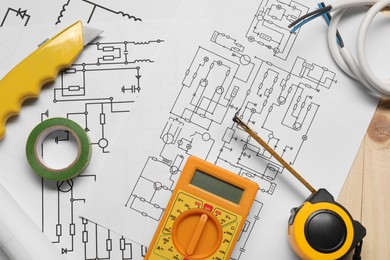 Wiring diagrams, wires and digital multimeter on wooden table, top view