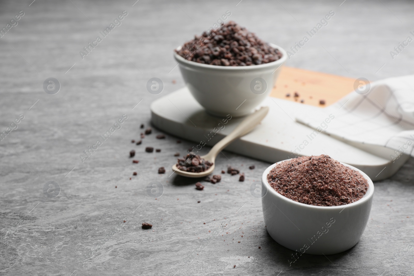 Photo of Ground black salt in bowl on grey table. Space for text