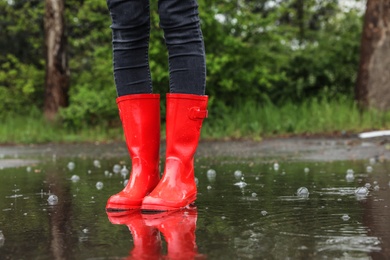 Woman in red rubber boots on rainy day outdoors, closeup