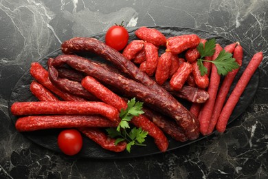 Photo of Thin dry smoked sausages, tomatoes and parsley on black marble table, top view