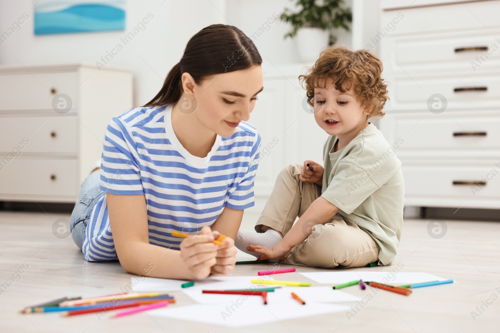 Photo of Mother and her little son drawing with colorful markers on floor at home