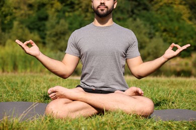 Man practicing yoga on mat outdoors, closeup. Lotus pose