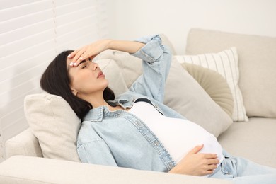 Photo of Pregnant woman suffering from headache on sofa at home