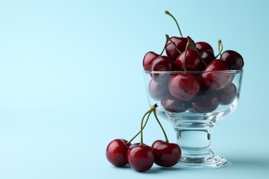 Photo of Fresh ripe cherries on light blue background, space for text