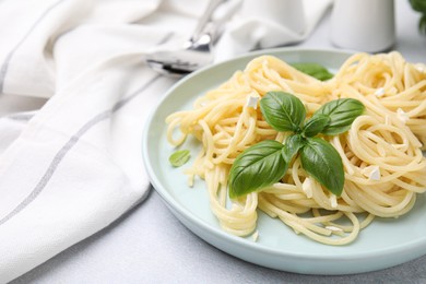 Photo of Delicious pasta with brie cheese and basil leaves on light grey table, closeup. Space for text
