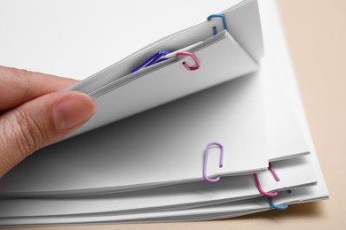 Photo of Woman stacking sheets of paper with clips on beige background, closeup