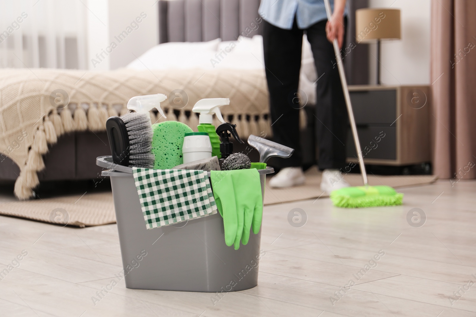 Photo of Woman cleaning floor, focus on different supplies in bucket at home