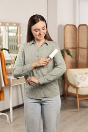 Photo of Young woman cleaning clothes with adhesive lint roller indoors