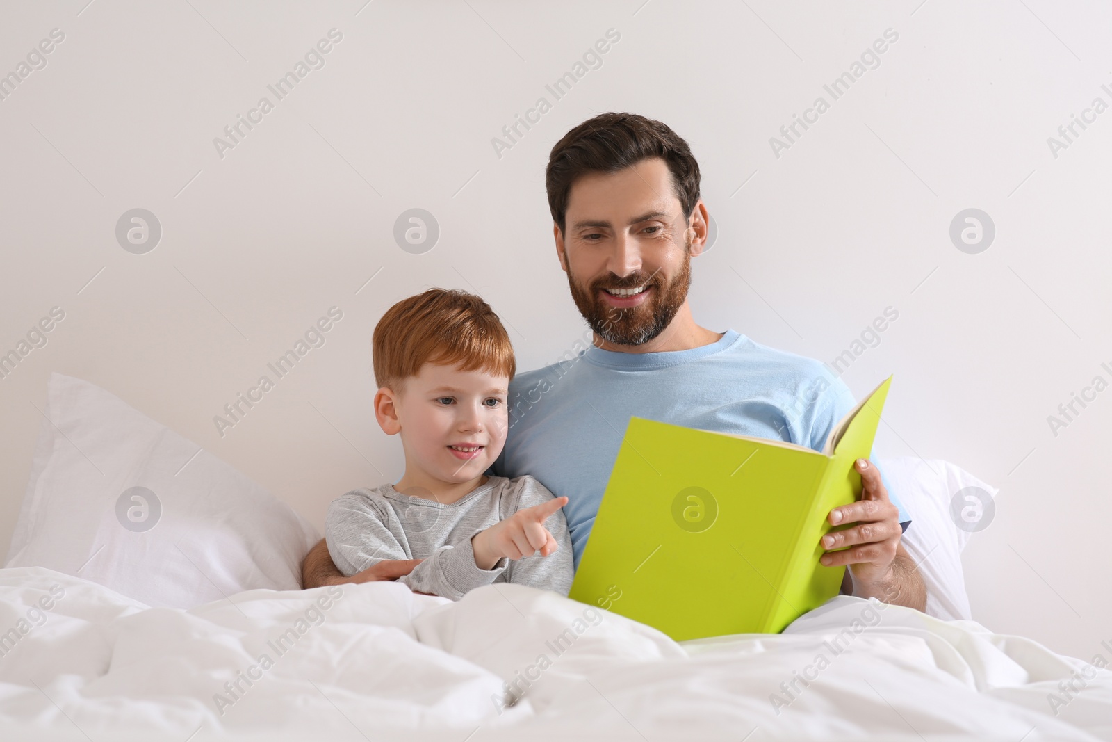 Photo of Father reading book with his child on bed at home