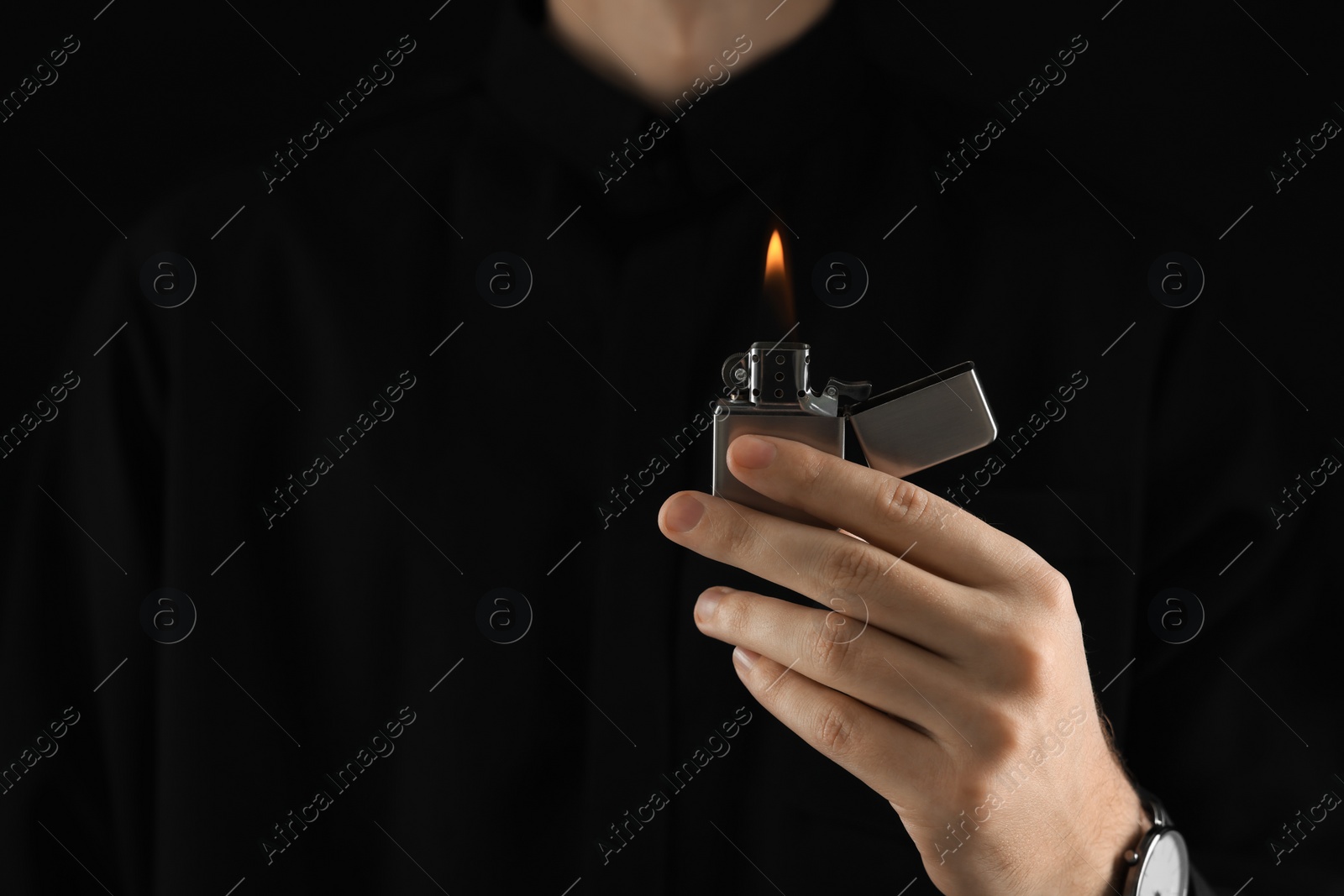 Photo of Man holding lighter with burning flame on black background, closeup. Space for text