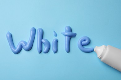 Photo of Word White written with toothpaste and tube on light blue background, flat lay
