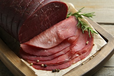 Photo of Tasty bresaola, peppercorns and rosemary on wooden table, closeup