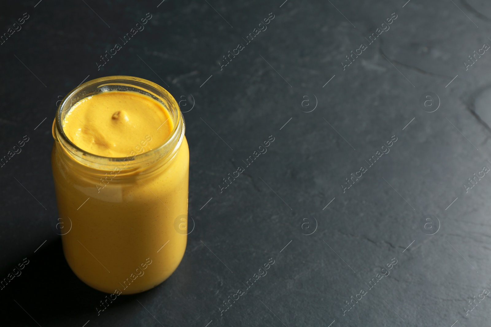 Photo of Spicy mustard in glass jar on black table. Space for text