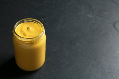 Spicy mustard in glass jar on black table. Space for text