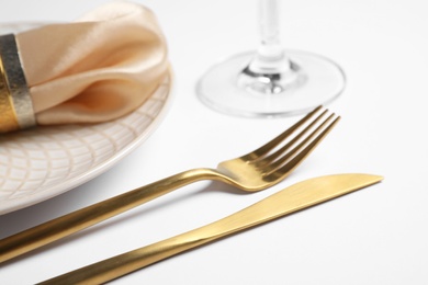 Beautiful table setting with golden cutlery and beige napkin on white background, closeup