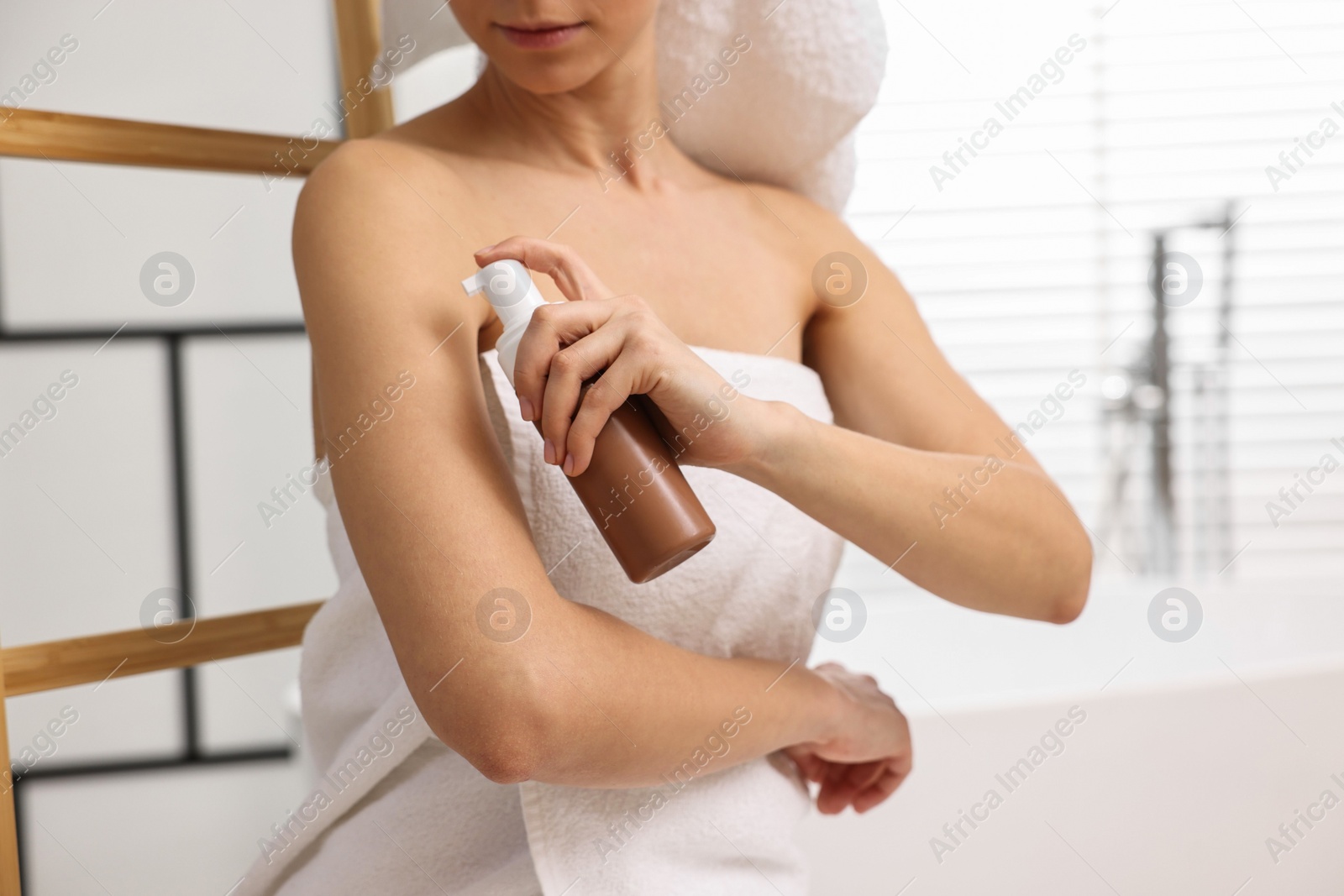 Photo of Woman applying self-tanning product onto arm in bathroom, closeup