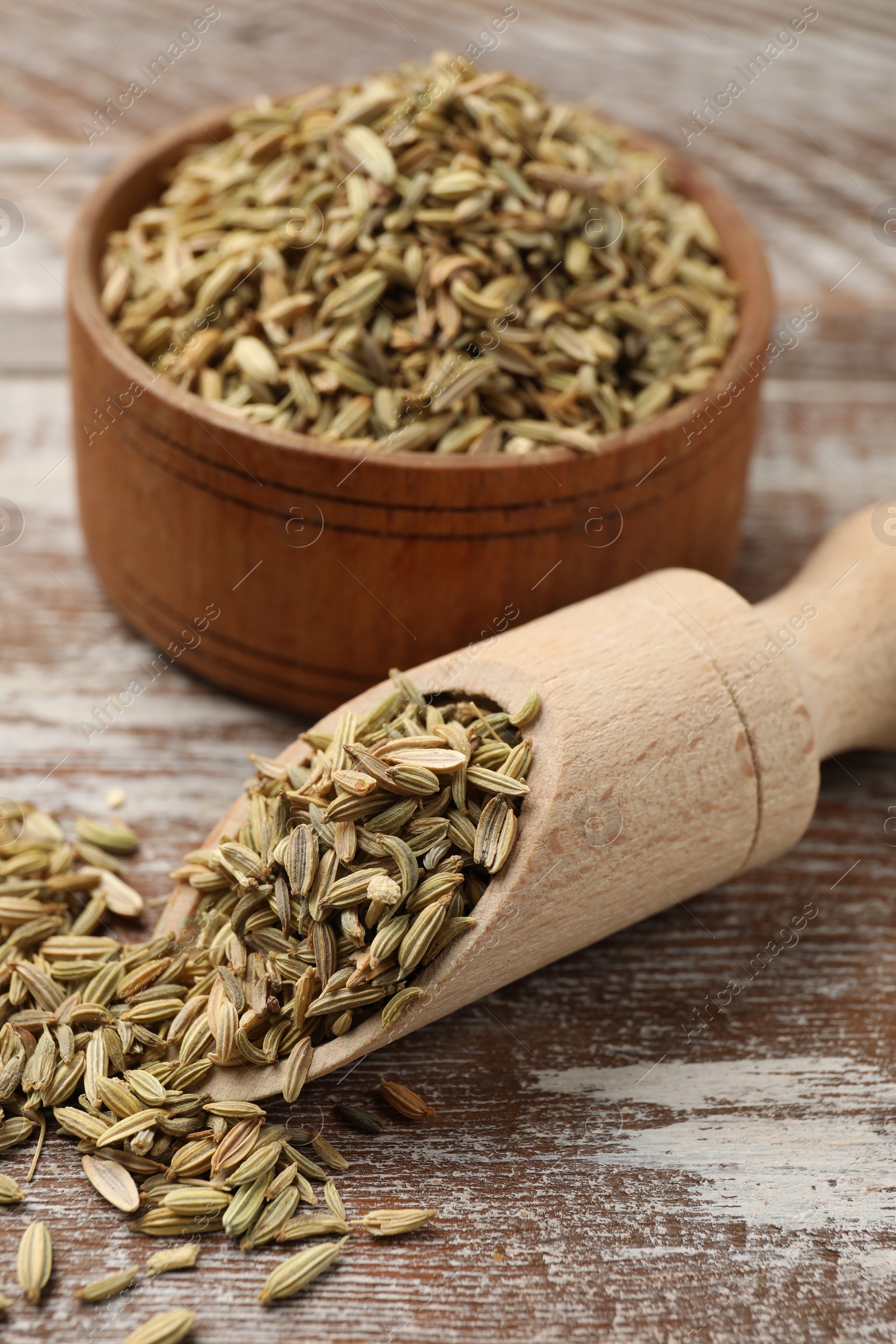 Photo of Bowl and scoop with fennel seeds on wooden table, closeup