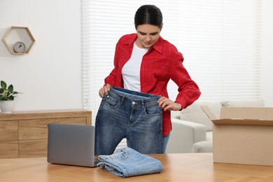 Young woman with just unpacked new jeans and laptop on wooden table indoors. Online shopping