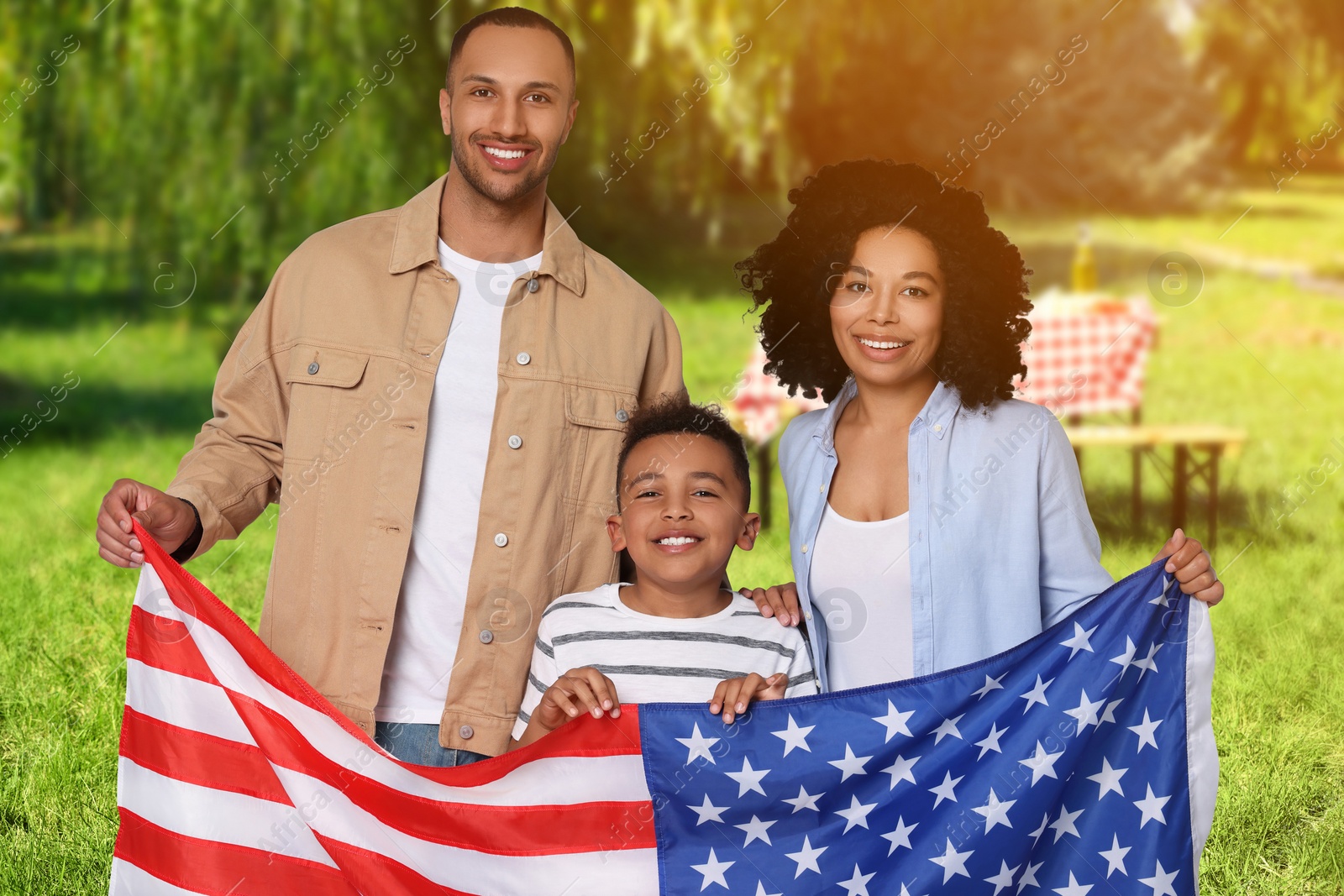 Image of 4th of July - Independence day of America. Happy family with national flag of United States having picnic in park