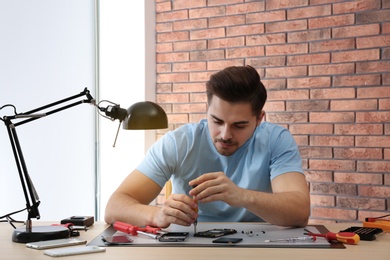 Photo of Technician repairing broken smartphone at table in workshop