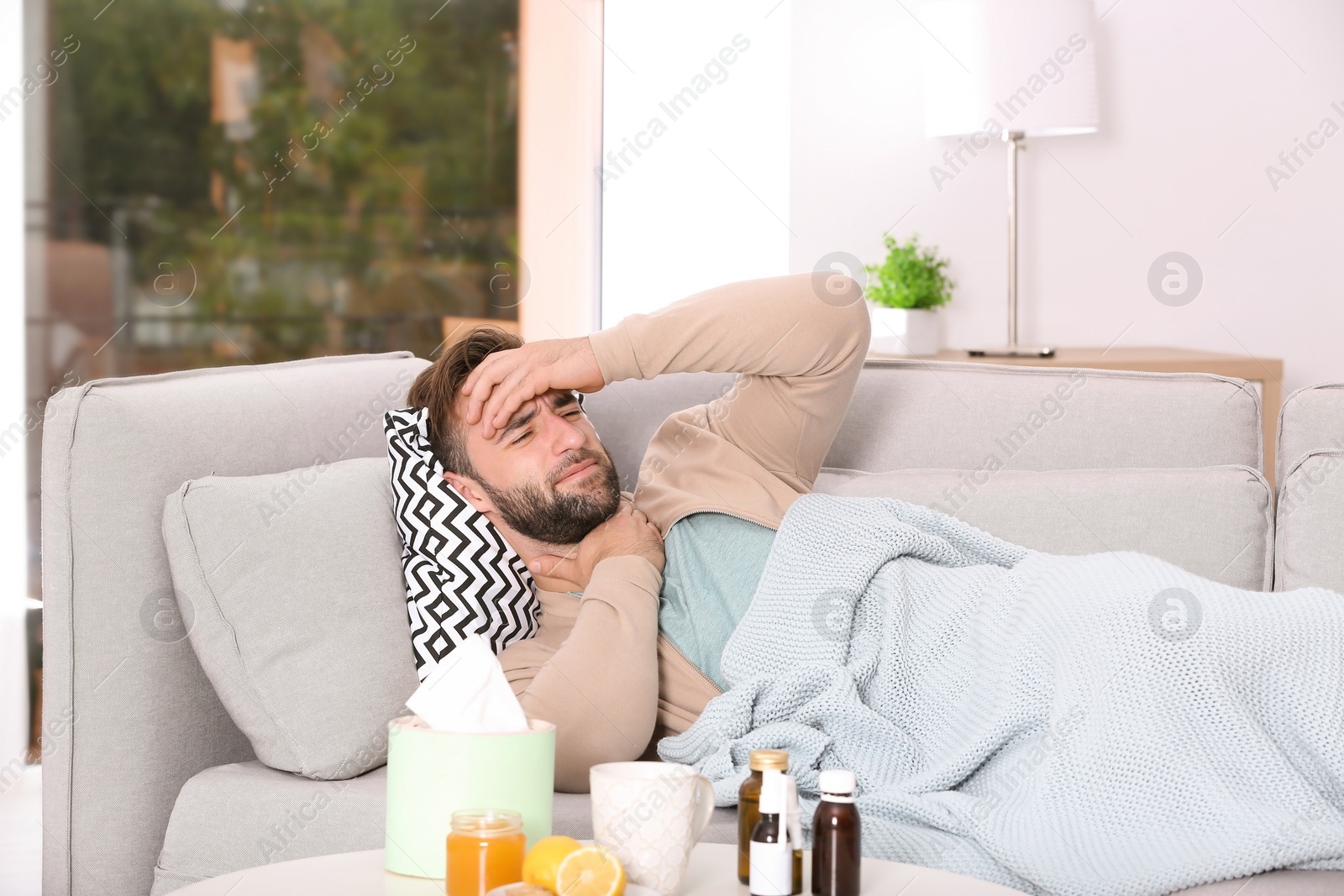 Photo of Ill man suffering from cough on sofa at home