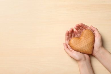 Woman holding heart on wooden background, top view with space for text. Donation concept