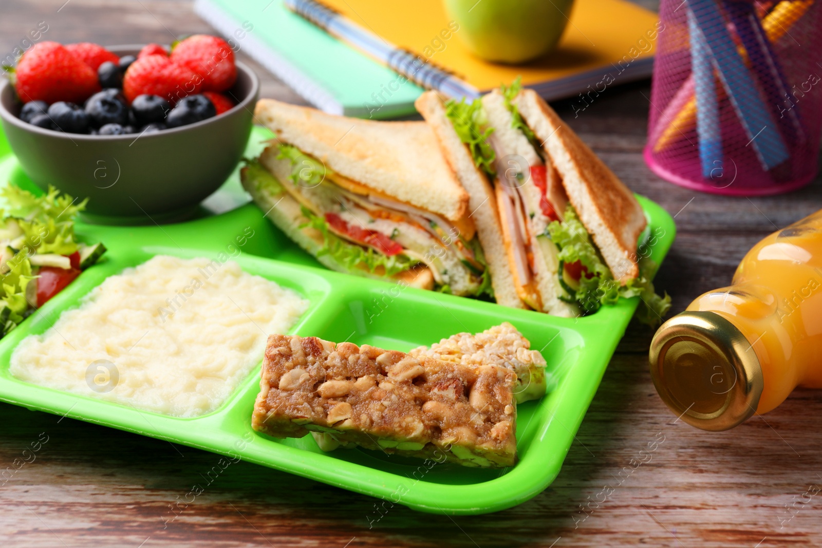 Photo of Serving tray of healthy food and stationery on wooden table. School lunch