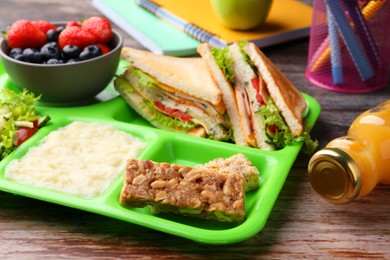 Photo of Serving tray of healthy food and stationery on wooden table. School lunch